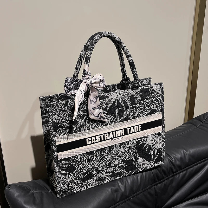 Black floral-patterned tote bag with 'Castrainn Tade' branding on a black surface.