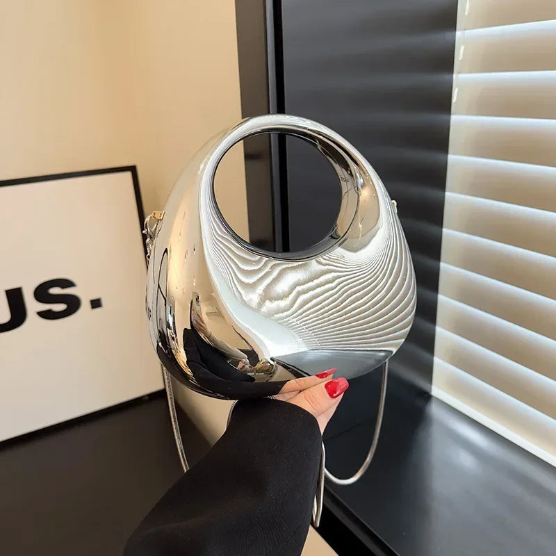 Silver handbag held by a hand with red nail polish against a blurred indoor background