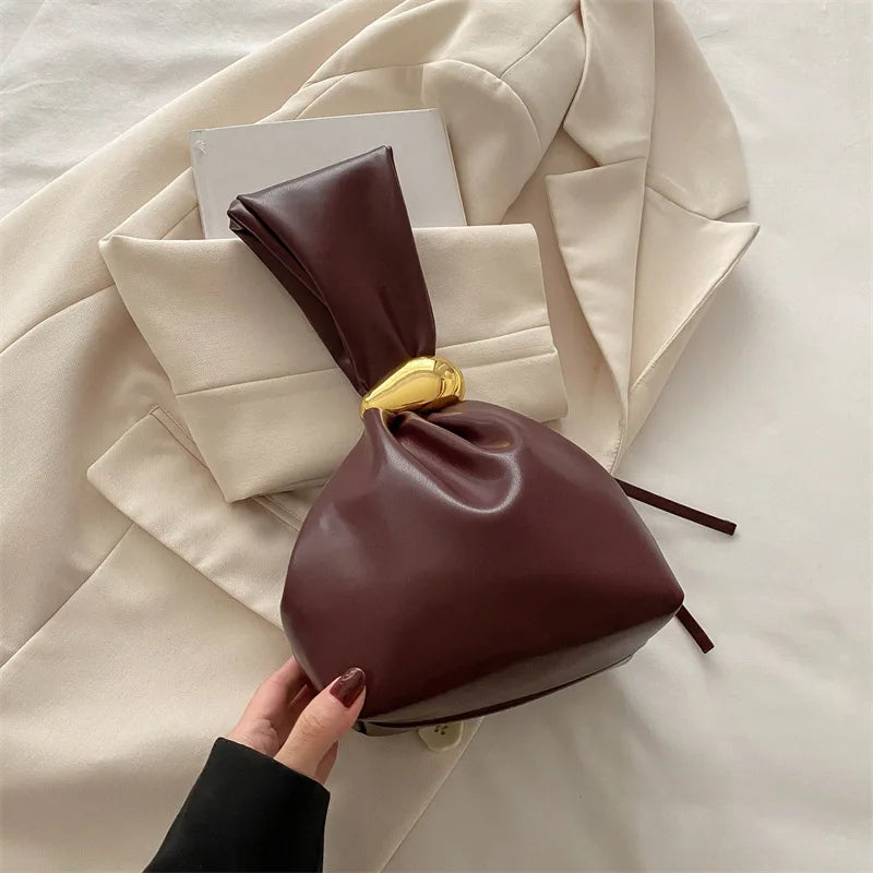 Brown leather drawstring bag held by a hand against a beige coat background