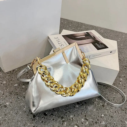 Silver Carauana UNIU Aurora Clutch handbag with gold chain handle on a concrete surface