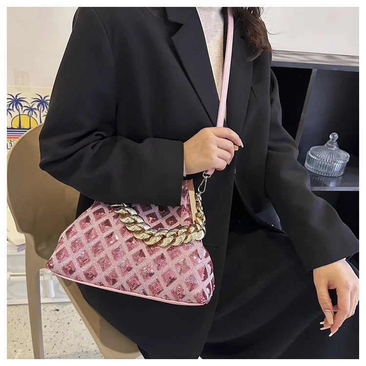 Person holding a pink handbag with gold chain detail, wearing a black suit.