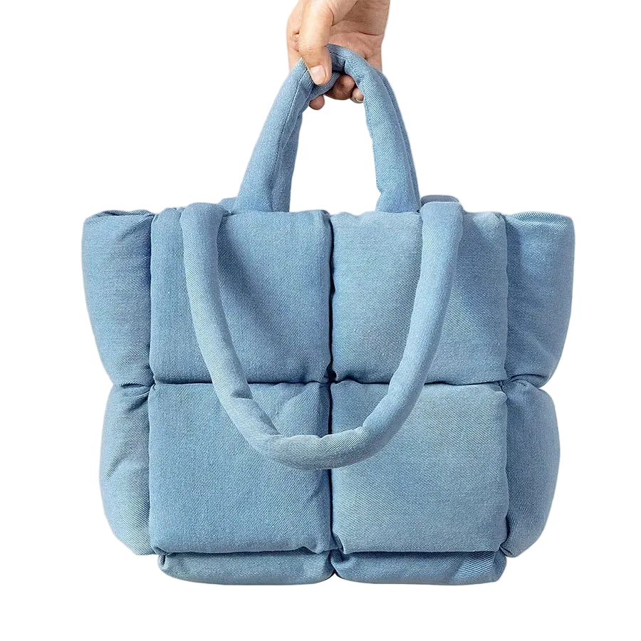 Blue quilted handbag held by a hand on a white background