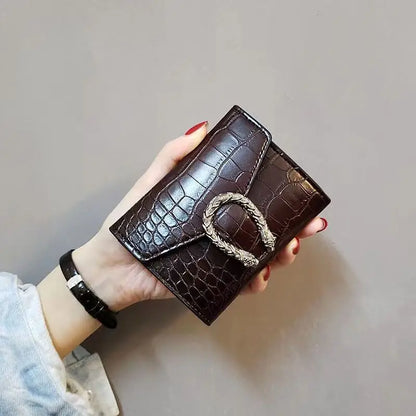 Hand holding a brown crocodile-patterned wallet with a decorative buckle black color